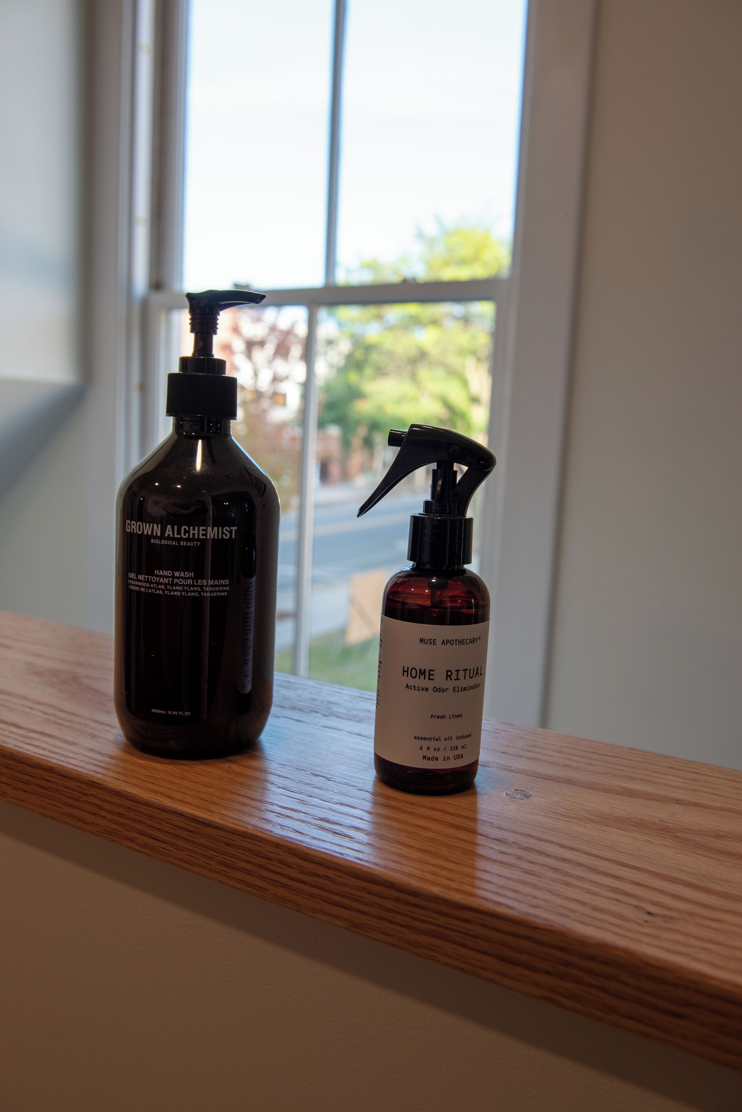 Two bottles of hand wash on a wooden ledge by a window.