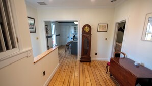 Un couloir doté d’un plancher en bois, d’un banc en bois et d’une grande horloge en bois accrochée au mur.