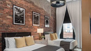 A hotel room with two beds, a brick wall, and framed pictures. - French’s Loft | Luxe Stay Near Broadway (Nashville)