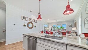 Une cuisine moderne avec des meubles blancs, un plan de travail en marbre et des luminaires suspendus rouges.