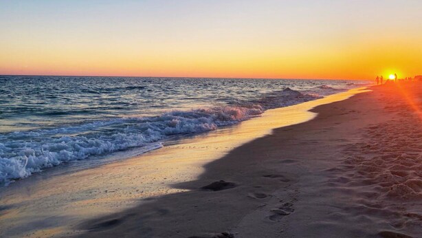 Une plage au coucher du soleil, avec des vagues et des empreintes de pas dans le sable.