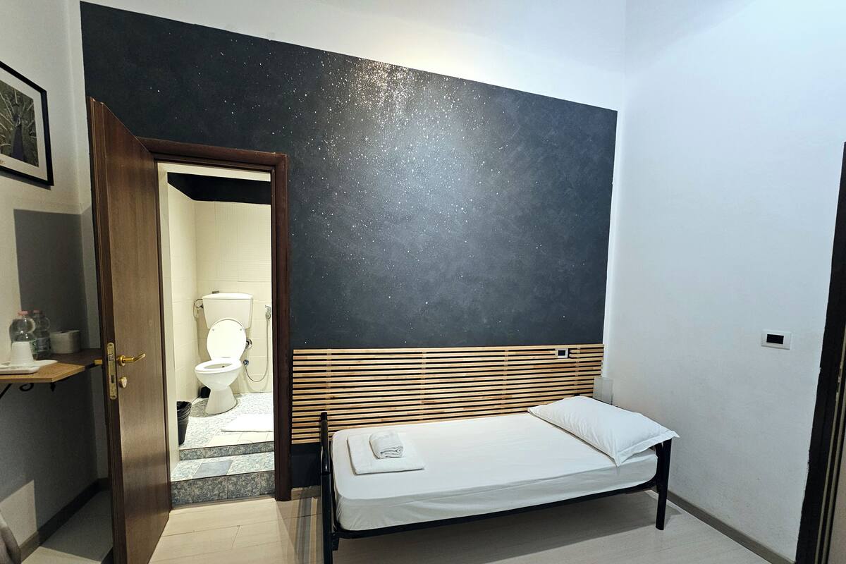 Une pièce comprenant un lit, une tête de lit en bois, un mur de couleur sombre et une porte donnant sur une salle de bain.