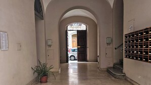 Un pasillo con suelo de baldosas, un arco de entrada, una planta en maceta y una escalera con barandilla de metal.