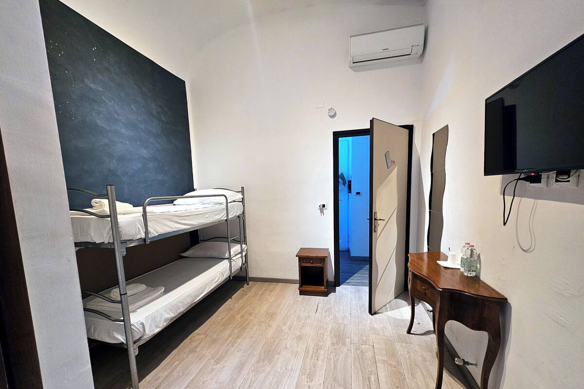 Une chambre de dortoir avec des lits superposés, un petit bureau en bois, un miroir, une télévision et un appareil de climatisation.