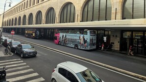 Una calle con un edificio grande que tiene ventanas de arco y un autobús con publicidad.