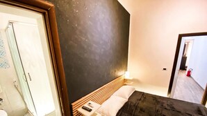 Un dormitorio con cama, mesita de noche con control remoto, pared con diseño de estrellas y baño con ducha e inodoro.