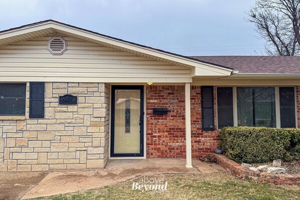 A two-story house with a stone facade, a front door, and a small porch. - The Spacious Avocado | 4 Bed, 2 Bath (Burkburnette)