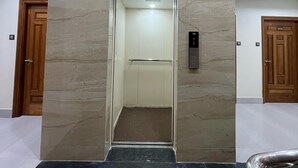 Um elevador com uma placa indicando o segundo andar, uma parede de mármore e uma porta de madeira à direita.