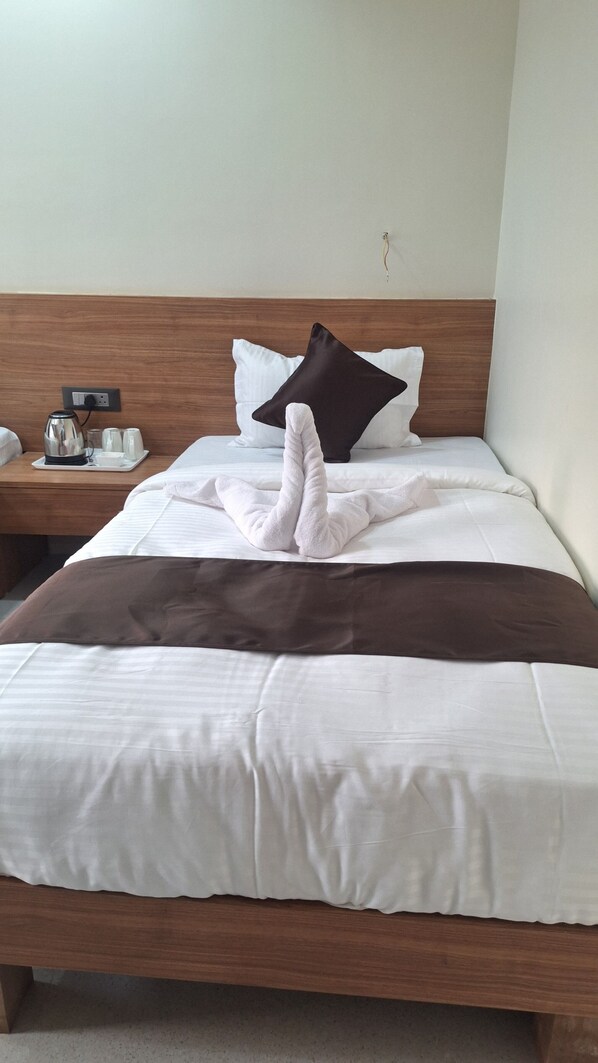 A neatly made bed with a brown blanket, white pillows, and a white towel folded in the center. - Hotel Momon (Guwahati)