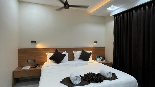 Quarto de hotel moderno com uma cama grande, um ventilador de teto e uma mesa de cabeceira com telefone e papéis.