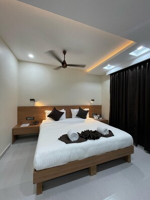A modern hotel room with a large bed, a ceiling fan, and a nightstand with a phone and papers. - Hotel Momon (Guwahati)