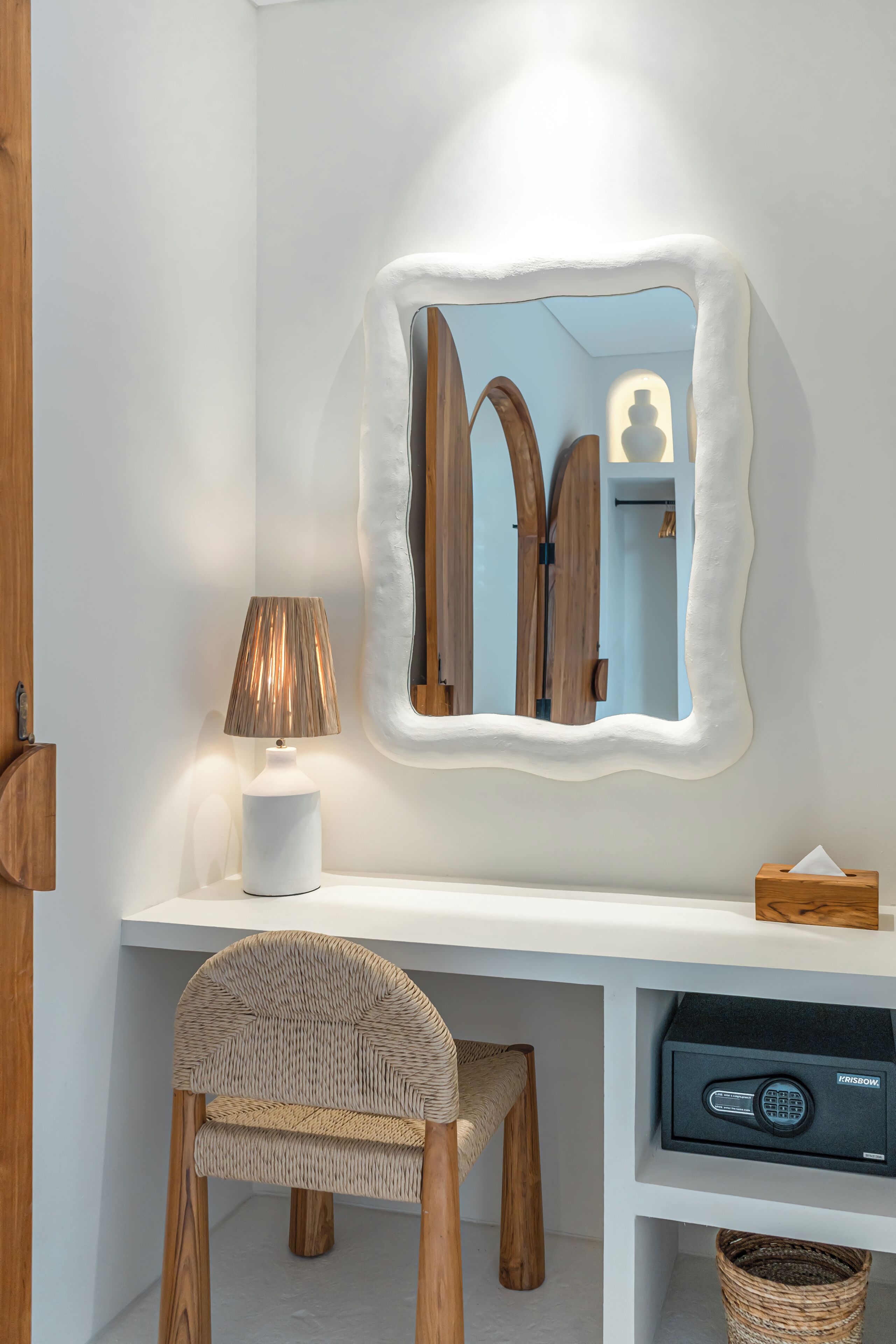 A white desk with a lamp, a chair, a mirror, and a safe.