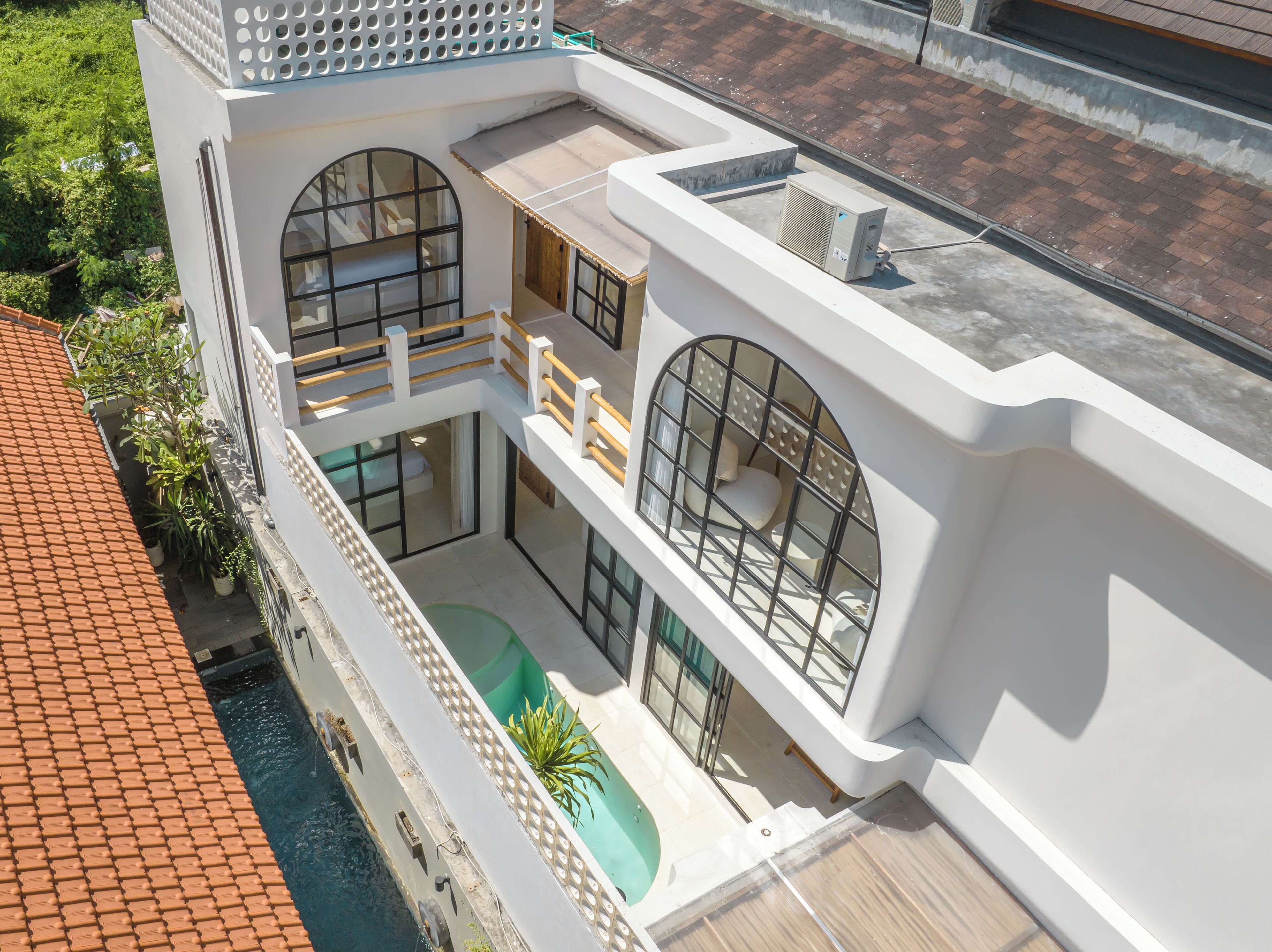Ein modernes, mehrstöckiges Gebäude mit Pool auf dem Dach, großen Bogenfenstern und einem Balkon mit Geländer.