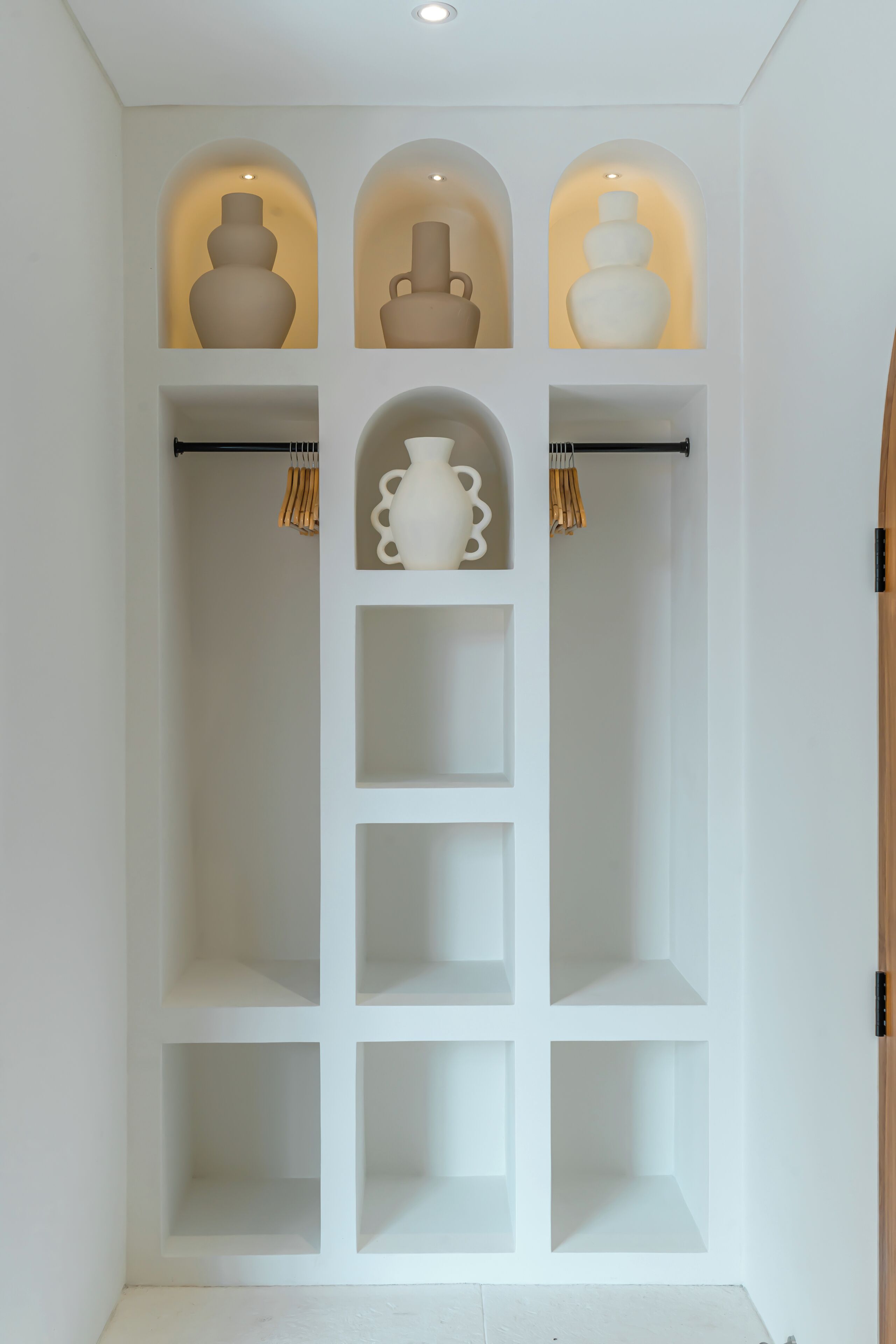 A white shelving unit with multiple compartments, some with vases and hanging clothes.