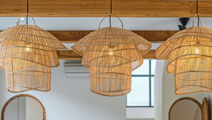 Ein modernes Interieur mit einem Holzesstisch, weißer Bettwäsche und drei gewebten Pendelleuchten.