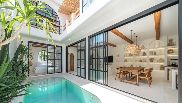 Ein modernes Haus mit Swimmingpool, Essbereich und durch große Glasüren einsehbarer Küche.