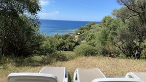 Zwei weiße Lounge-Stühle mit Blick auf das Meer und viel Grün.
