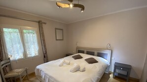 Ein ordentlich bezogenes Bett mit Handtüchern, einem Sessel, einem Nachttisch und einem Deckenventilator in einem gut beleuchteten Zimmer mit Fenster.