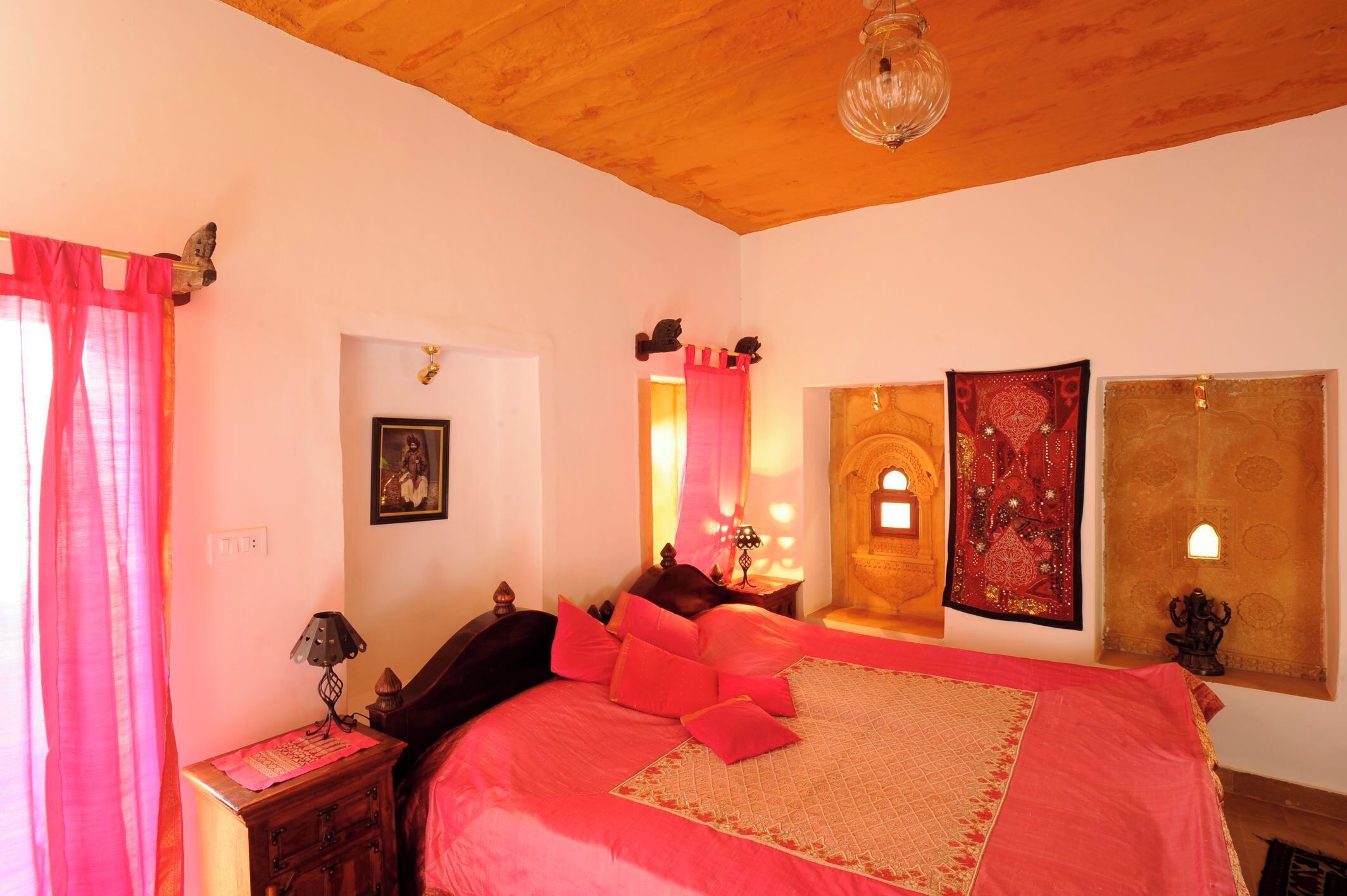 A bedroom with a large bed, a nightstand, a lamp, a mirror, and a tapestry on the wall.