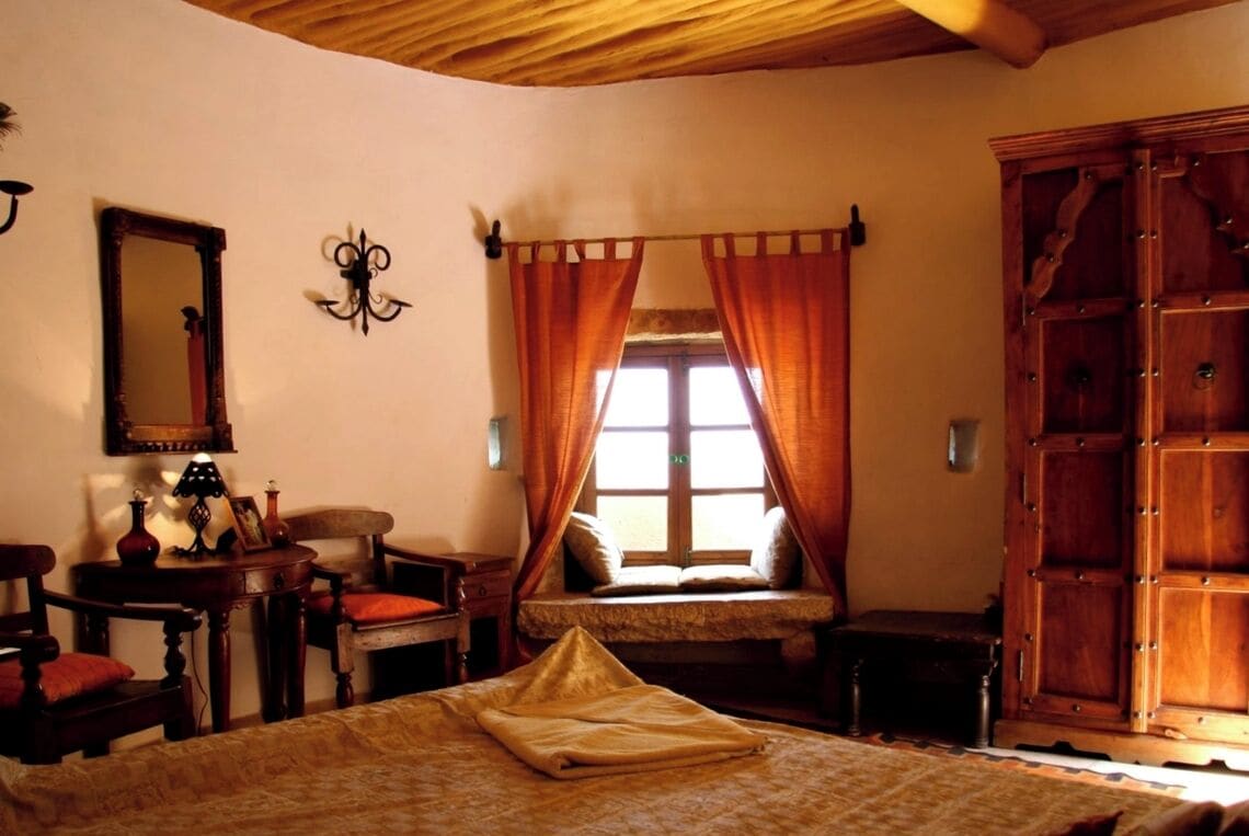Ein gemütliches Zimmer mit Bett, Sessel, kleinem Tisch, Spiegel und Kleiderschrank.
