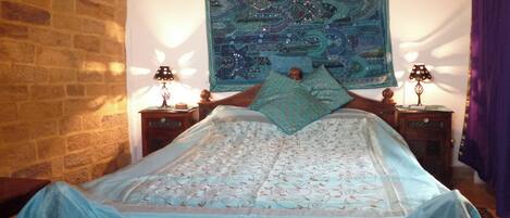 A bed with a patterned bedspread, two bedside tables with lamps, a tapestry on the wall, and a brick wall.