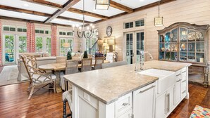 A spacious kitchen with a large island, wooden beams, and a dining area with wicker furniture. - WaterColor Retreat with Beach Club Access, Golf Cart, and Private Pool for the Ultimate Escape! (Seagrove Beach)