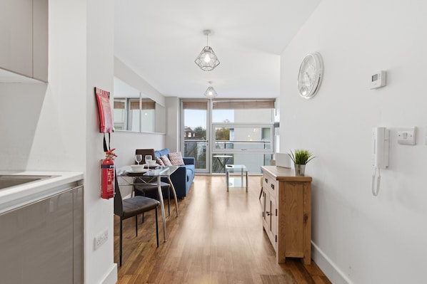 A modern kitchen with a dining area, wooden cabinets, a fire extinguisher, and a clock on the wall.