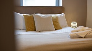 A neatly made bed with a headboard, pillows, and a folded towel. - Properties Unique | Cherry (Newcastle Upon Tyne)