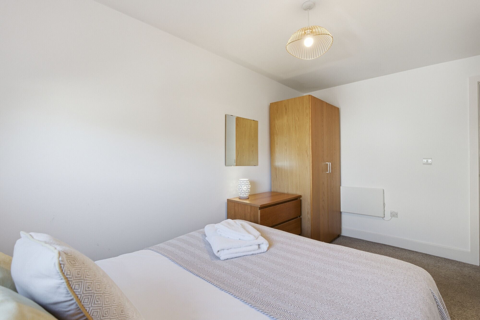 Un dormitorio con cama, armario de madera, mesita de noche con lámpara y espejo en la pared.