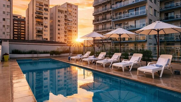 Une piscine sur le toit, agrémentée de chaises longues et de parasols, entourée d’immeubles de grande hauteur.