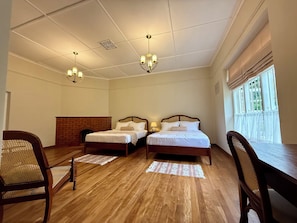 Une chambre d’hôtel avec deux lits en bois, une cheminée en briques et une grande fenêtre ornée de rideaux légers.