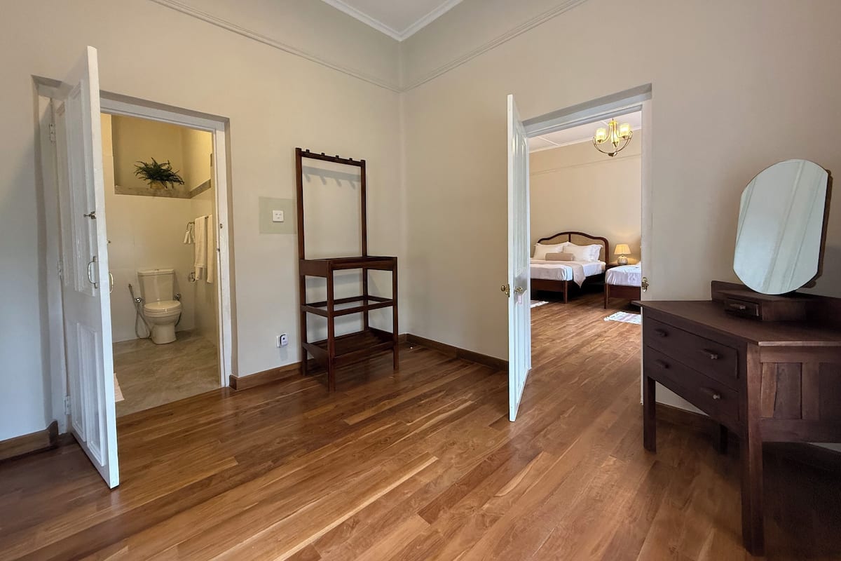 Une pièce avec un plancher en bois, une chaise en bois, une commode avec un miroir et un lit avec une table de chevet.