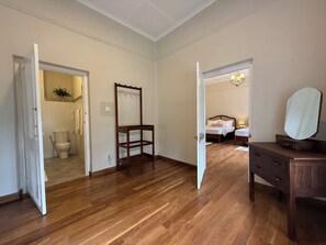 Une pièce avec un plancher en bois, une chaise en bois, une commode avec un miroir et un lit avec une table de chevet.