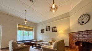 Un salon spacieux avec une cheminée, deux fauteuils, un canapé, une table basse et une grande horloge murale.