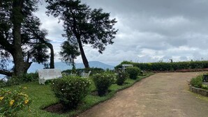 A gravel path leading to a bench and a gazebo in a landscaped garden with trees and shrubs. - The Gundumalai Bungalow  (Suryanelli)