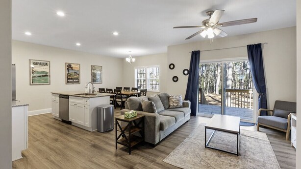 Een moderne woonkamer met keuken, eethoek en balkon met uitzicht op bomen.