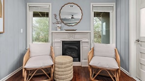 A room with a fireplace, two wicker chairs, a mirror, and a window with blinds.