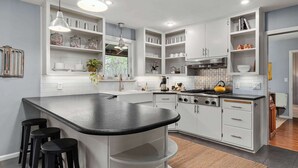 A modern kitchen with white cabinetry, a black countertop, and bar stools.