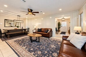 A spacious living room with a brown leather sofa, a round coffee table, and a dining area with a bench and table. - 7BR Villa w/ Pool, Cinema & Guest House | Tomball (Harris County)