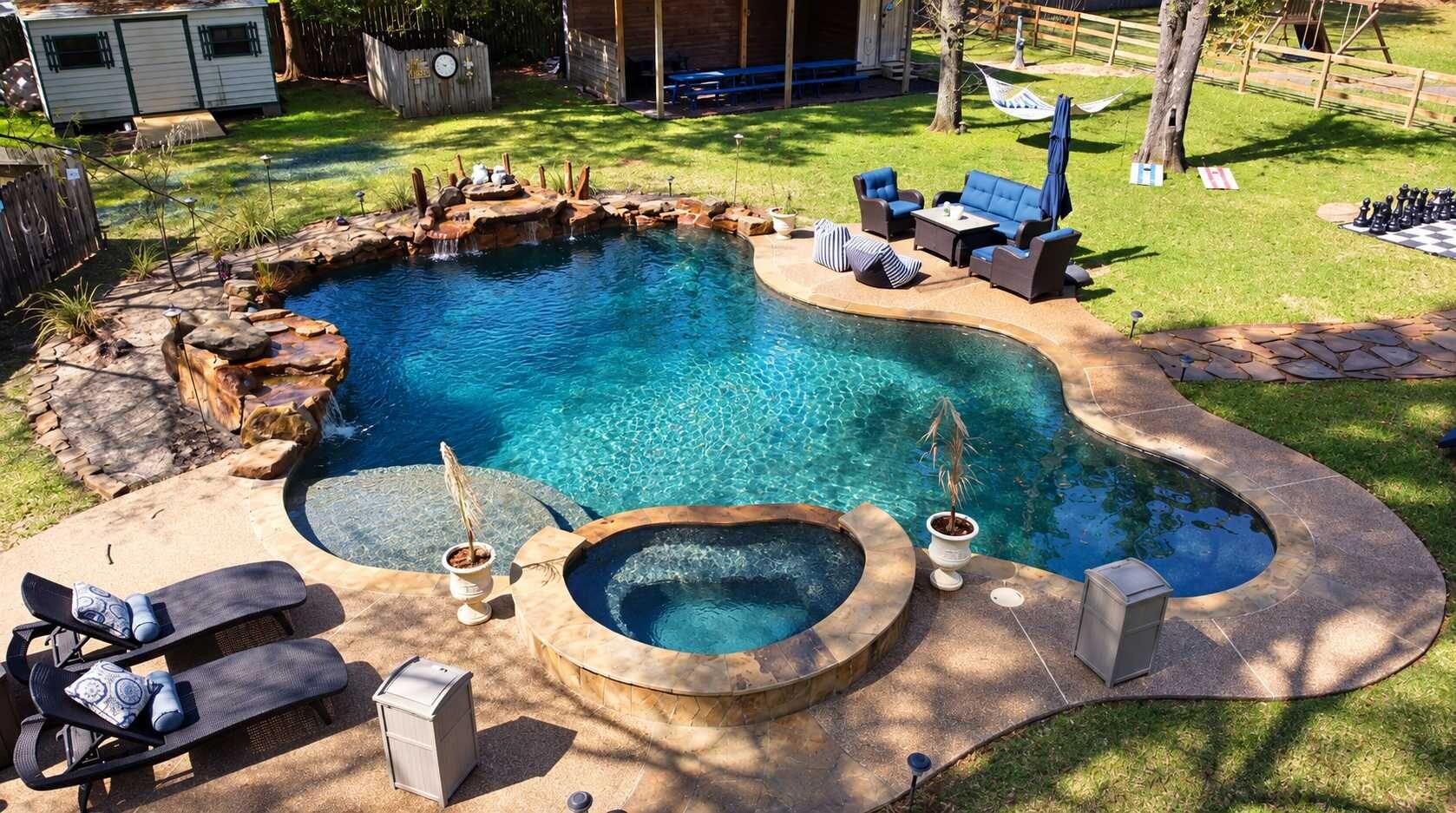 A swimming pool with a hot tub, lounge chairs, and a deck area.
