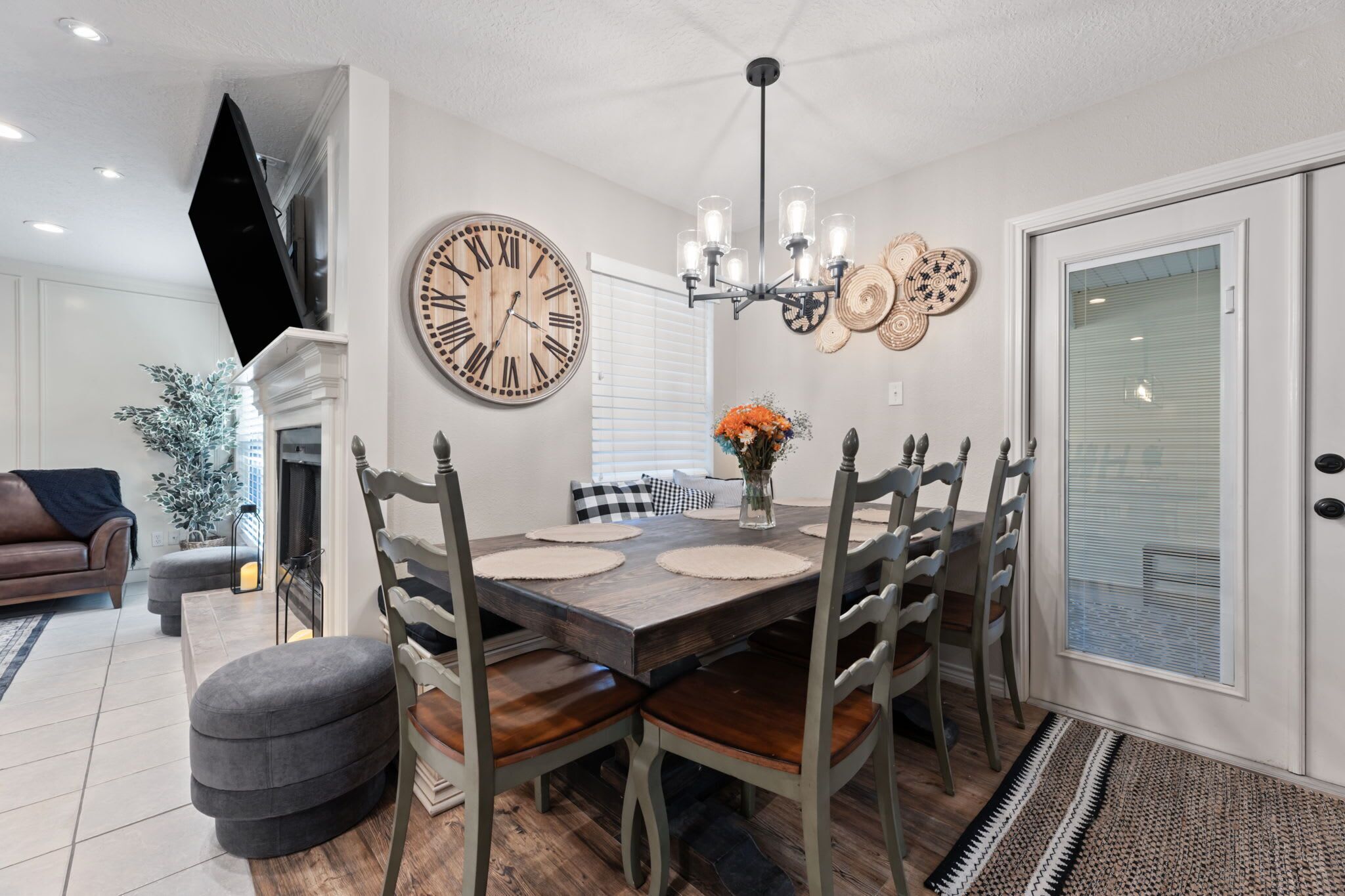 A dining area with a wooden table, six chairs, a large wall clock, and a chandelier.