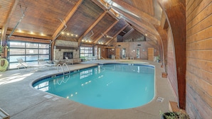 An indoor swimming pool with wooden beams, a stone fireplace, and lounge chairs. - Osage Beach Condo | Pools, Boatslip and Pickleball (Osage Beach)