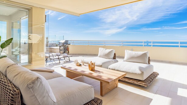 A balcony with a view of the sea, furnished with a sofa, a table, and a grill.
