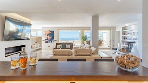 A modern living room with a large TV, seating area, and a view of the sea.
