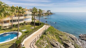 A coastal property with a pool, palm trees, and a view of the sea.