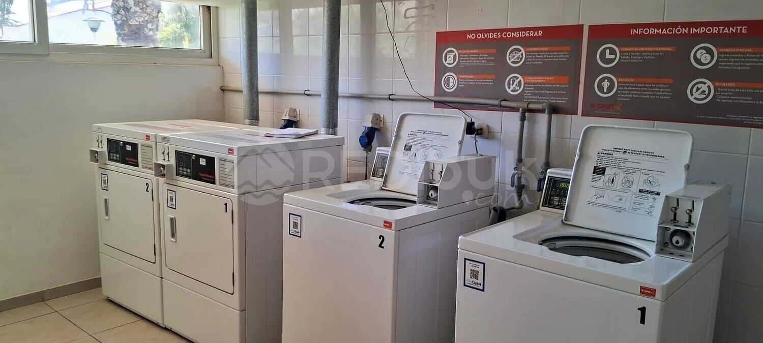 A laundry area with four washing machines and dryers, numbered 1 to 4. There are informational signs on the wall and a window providing natural light.