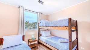 A room with bunk beds, a small bedside table with a lamp, and a window with a view of trees. - Increíble depto a pasos de Av. del Mar (La Serena)