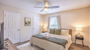Une chambre à coucher comprenant un lit, un ventilateur de plafond, une table de chevet, une lampe et un téléviseur.