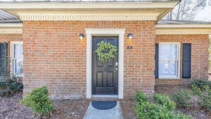 Une maison en briques avec une porte d’entrée sombre, une guirlande et un petit jardin agrémenté d’arbustes.