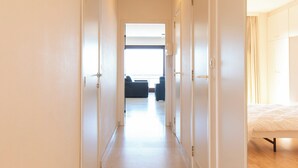 Ein Hotelgang mit weißen Wänden, einem gefliesten Boden und Türen zu einem Schlafzimmer mit Bett und Fenster.